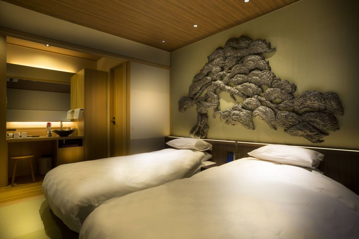 A hotel room with two beds, a desk with a chair, and a decorative wall piece.