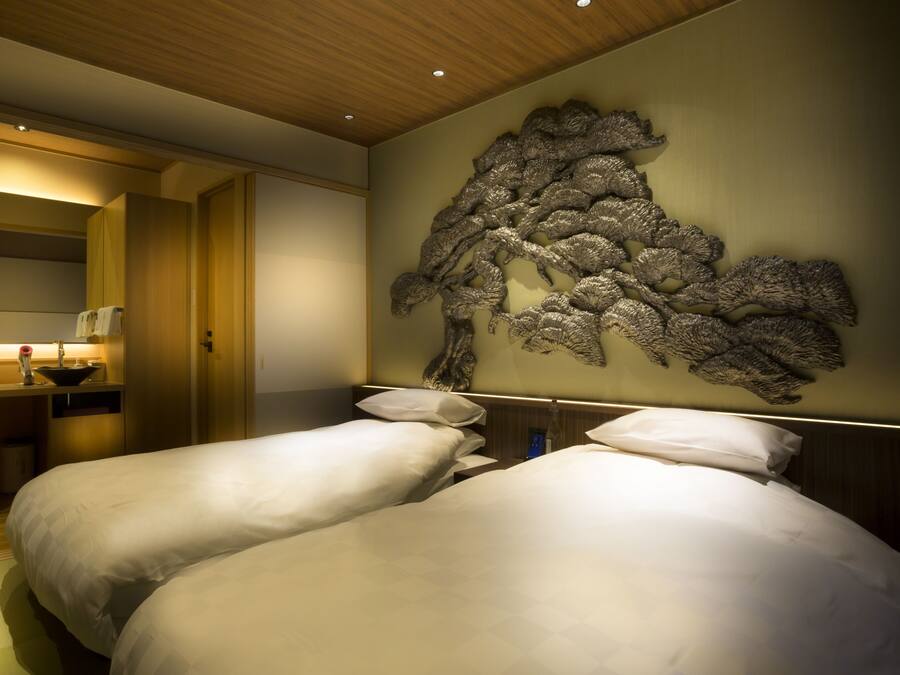 A hotel room with two beds, a desk with a chair, and a decorative wall piece.