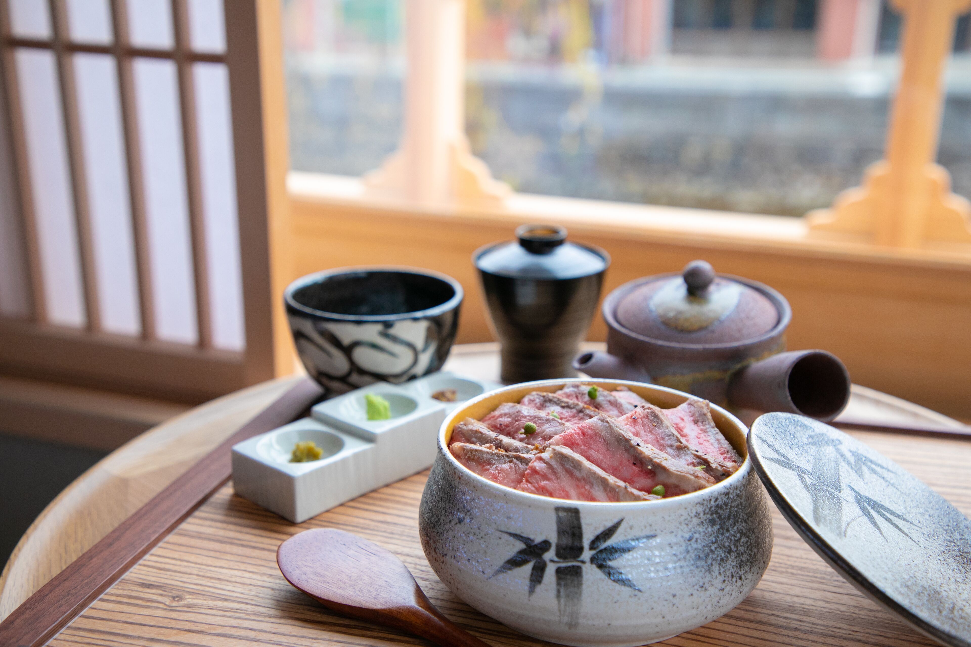 A traditional Japanese meal setup with a bowl of meat, chopsticks, and a tea set on a wooden tray.