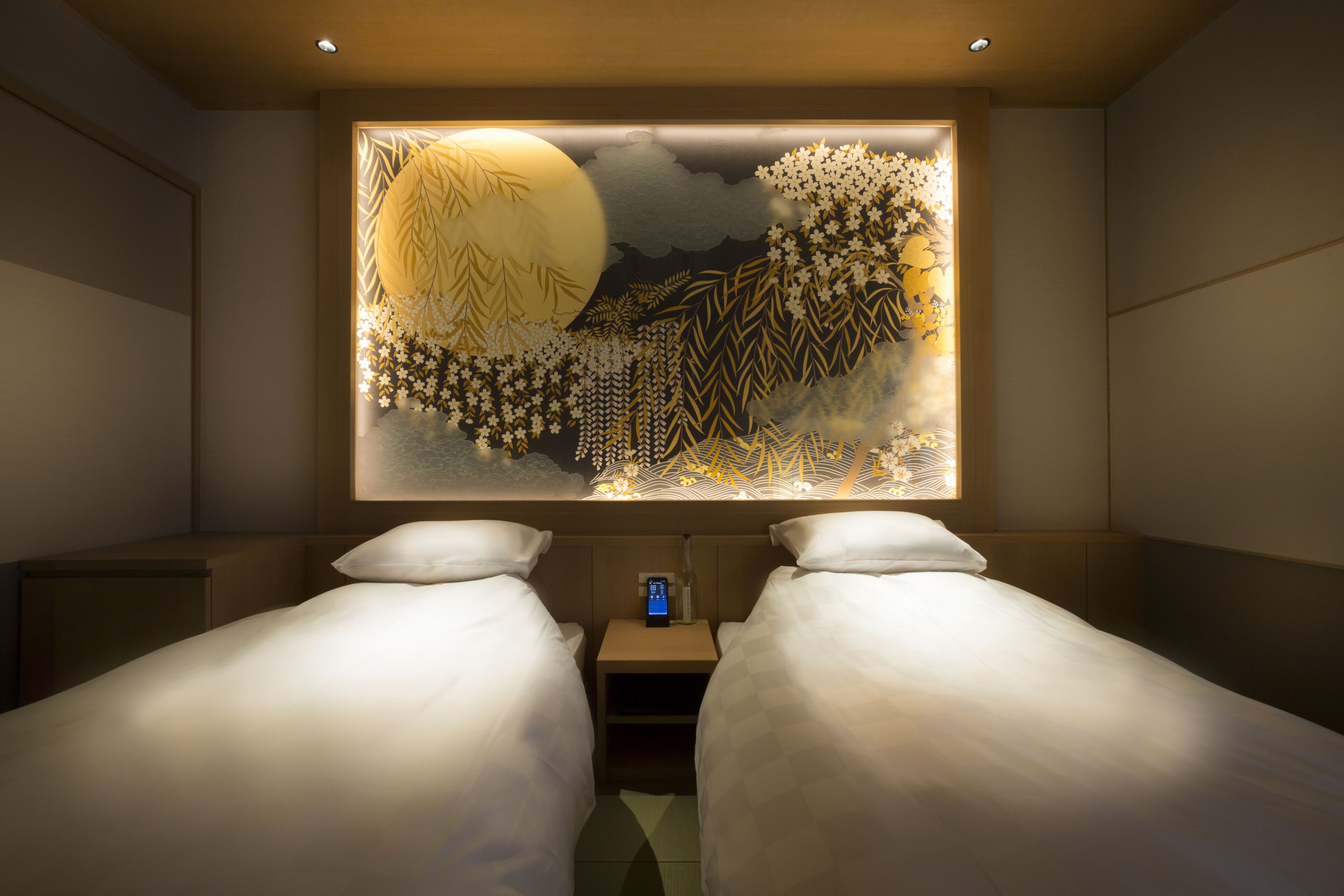 A hotel room with two beds, a nightstand with a digital clock, and a large illuminated wall art piece.