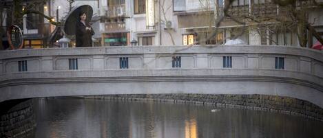 A stone bridge over a calm body of water with buildings in the background.