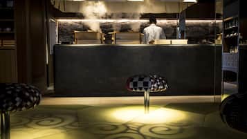 Un restaurante con una decoración moderna, que presenta una barra con una persona detrás y dos taburetes en primer plano.