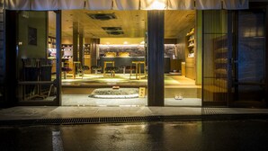 A hotel entrance with a wet pavement, a visible reception desk, and a large window displaying interior furnishings. - Sumihei Bettei Tokitotoki (Toyooka)