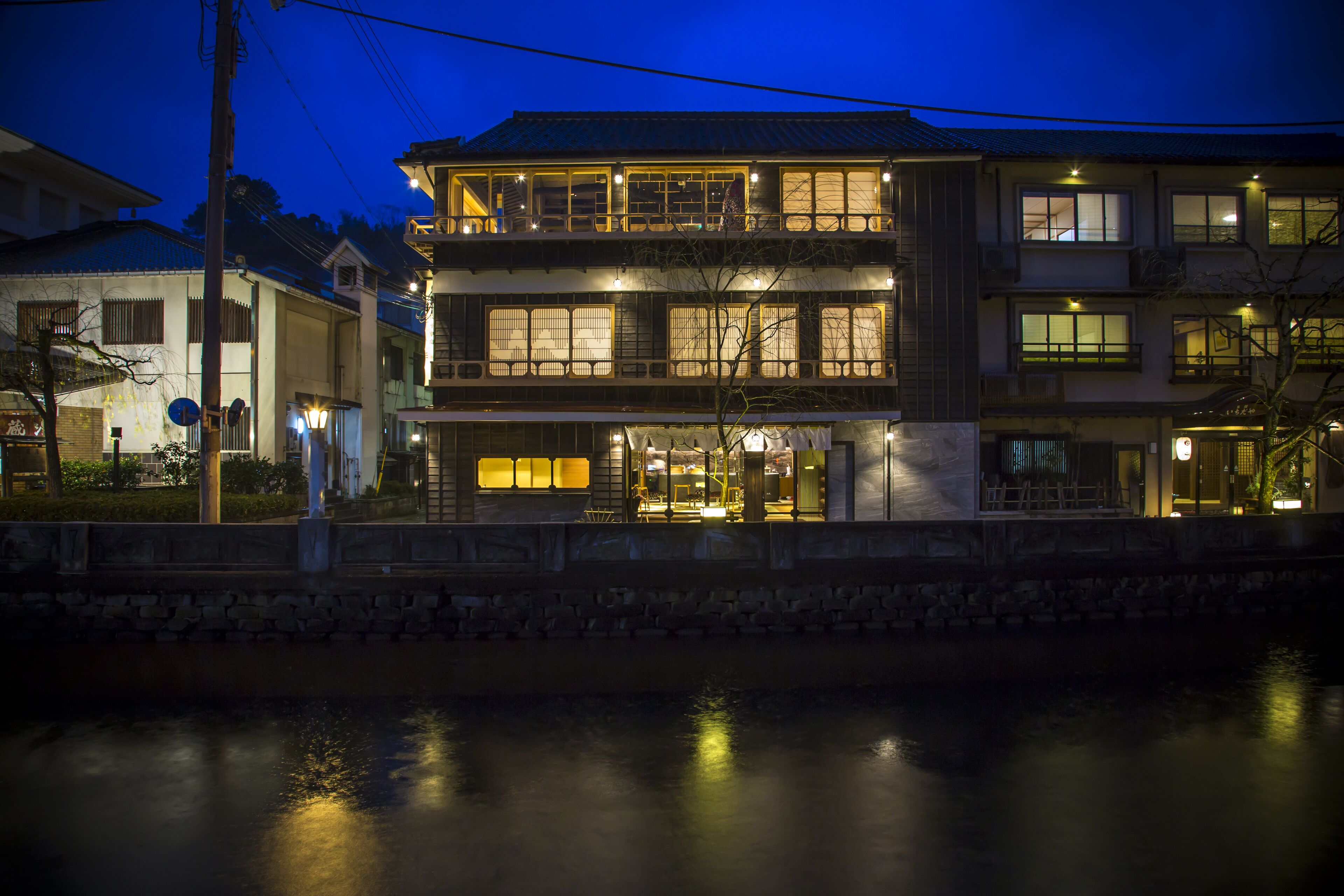 A traditional Japanese building with multiple floors, a stone wall in the foreground, and a river in the background.