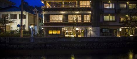 A traditional Japanese building with multiple floors, a stone wall in the foreground, and a river in the background.