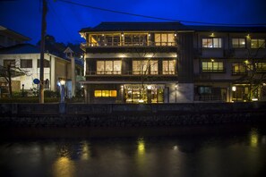 A traditional Japanese building with multiple floors, a stone wall in the foreground, and a river in the background. - Sumihei Bettei Tokitotoki (Toyooka)