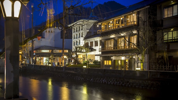 A riverside hotel with multiple floors, outdoor seating, and a stone wall along the water. - Sumihei Bettei Tokitotoki (Toyooka)