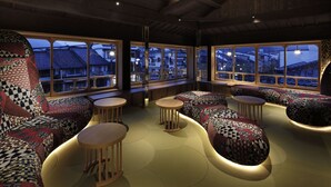 A cozy seating area with patterned cushions and round tables, large windows offering views of buildings outside. - Sumihei Bettei Tokitotoki (Toyooka)