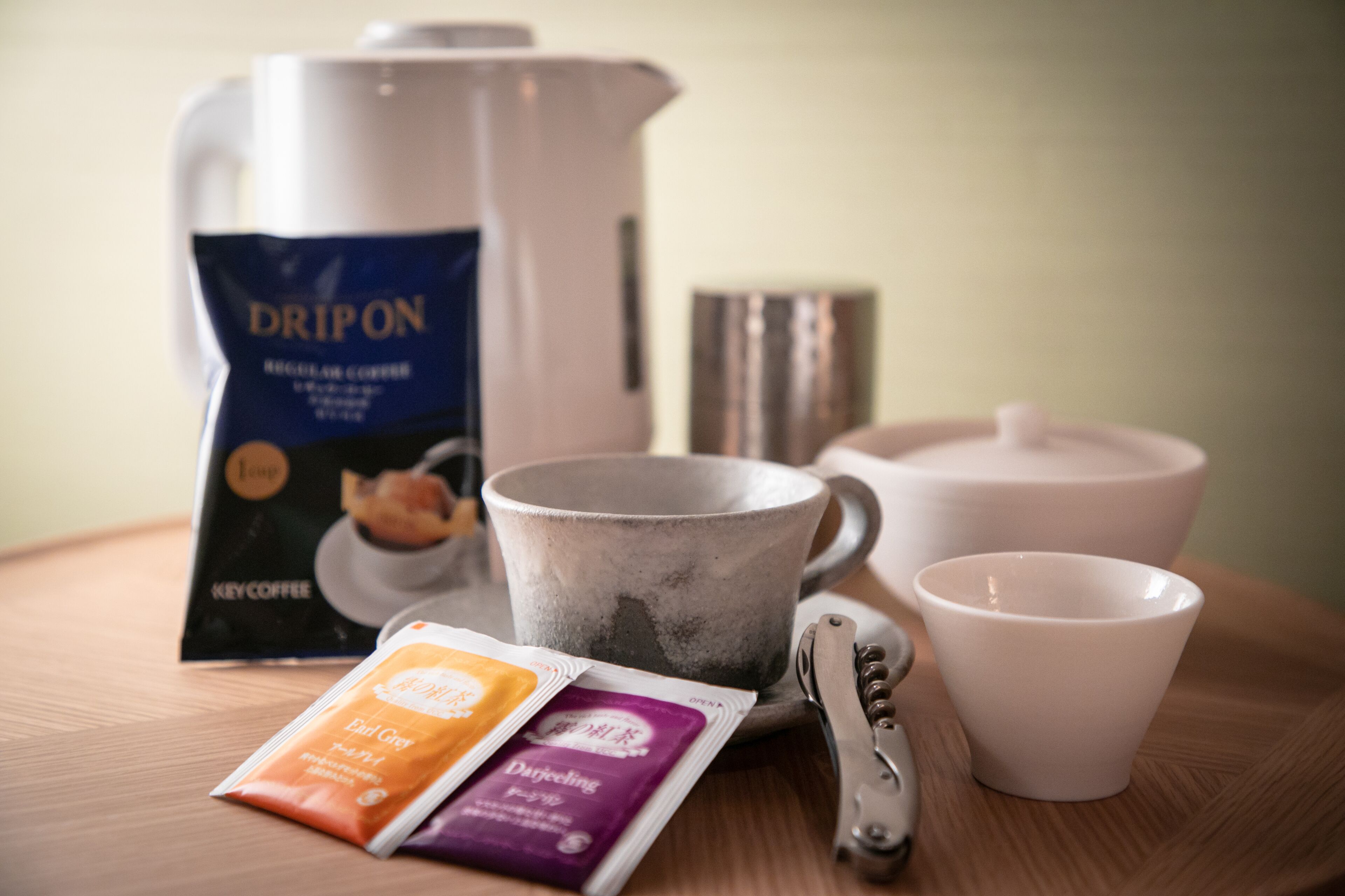 A coffee maker, a kettle, a cup, and a packet of coffee on a wooden table.