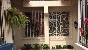 A courtyard with a tiled pathway, a potted plant, and a window with decorative bars. - Alquilo Apartamento Centro Guayaquil (Guayaquil)