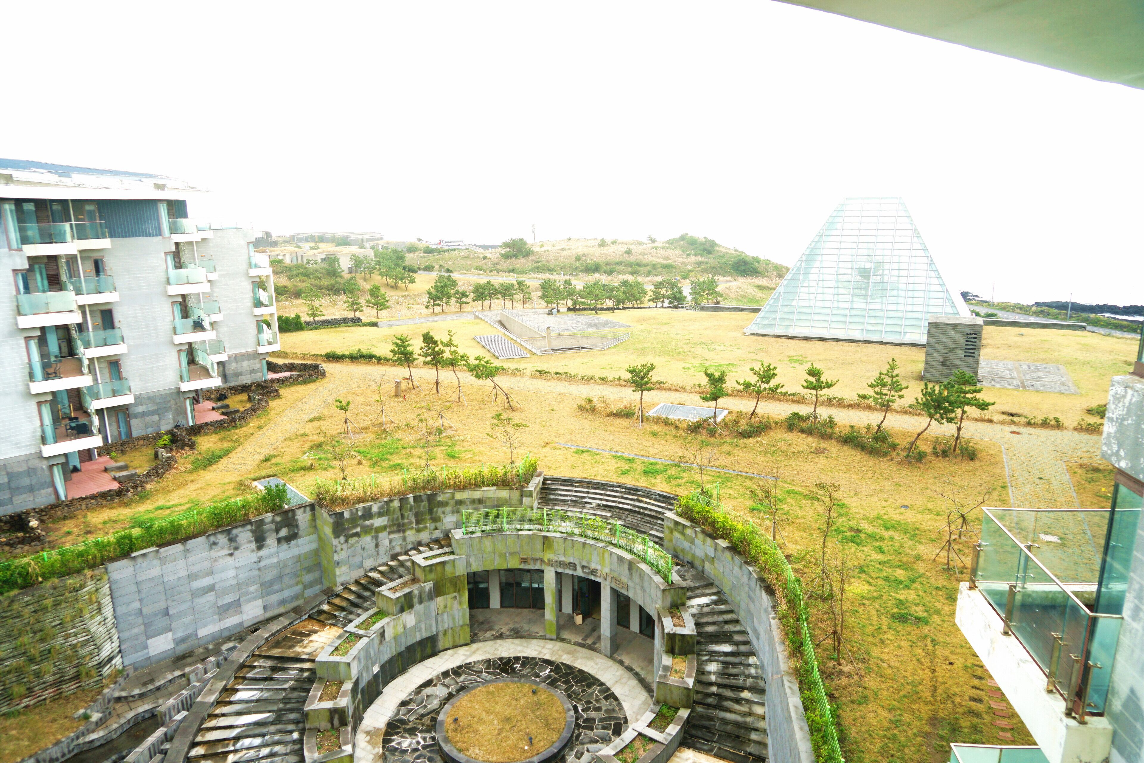 Um edifício moderno com um pátio circular, uma estrutura em forma de pirâmide de vidro e vista para uma paisagem montanhosa.