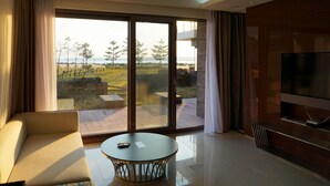 Un salon moderne doté d’une grande porte-fenêtre coulissante donnant sur un balcon, d’un canapé confortable, d’une table basse ronde et d’un téléviseur à écran plat.