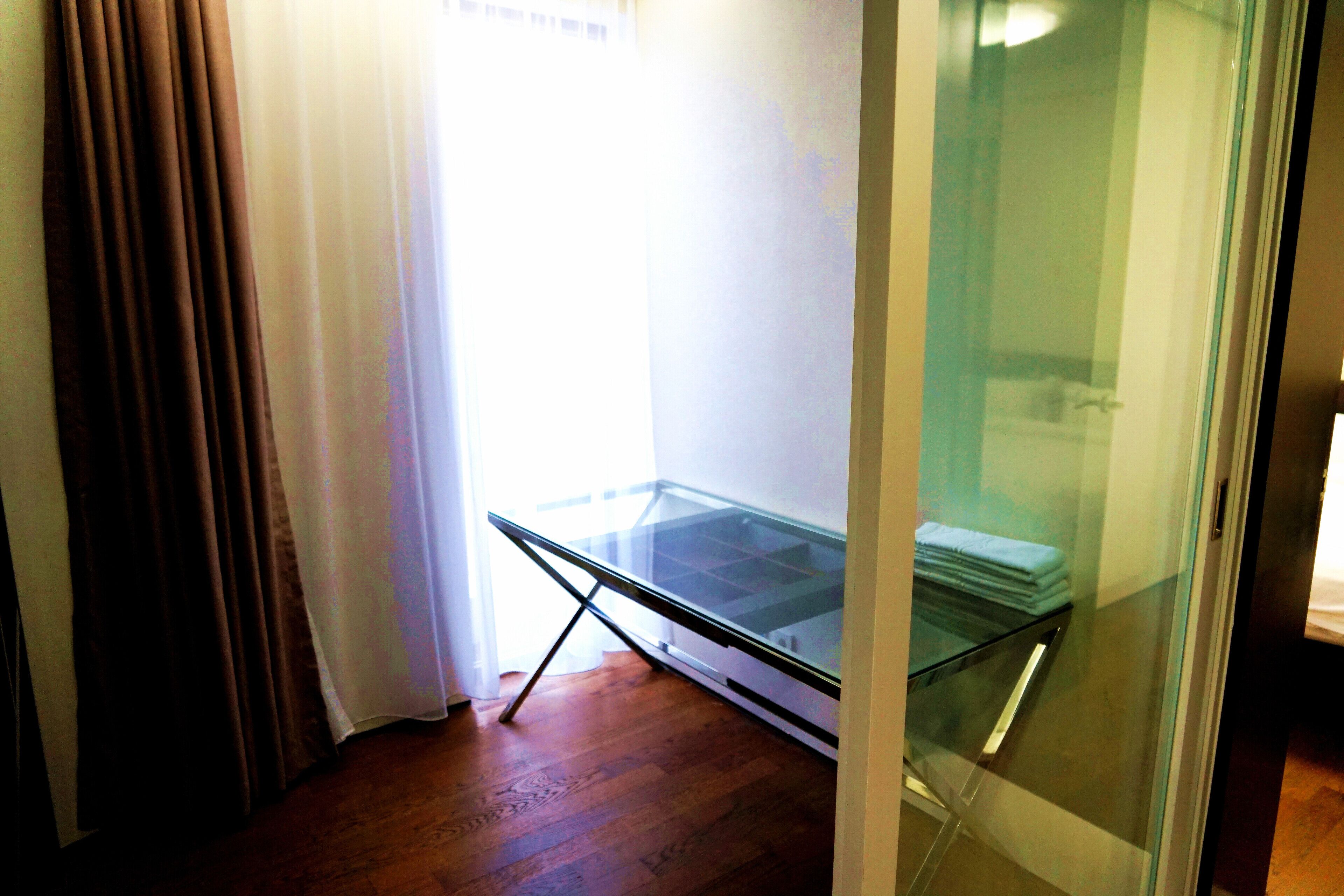 A room with a glass-top table, wooden flooring, and a glass partition.