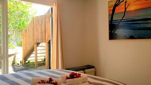 A bedroom with a bed, a painting of a sunset, and a view of a wooden deck and greenery outside.