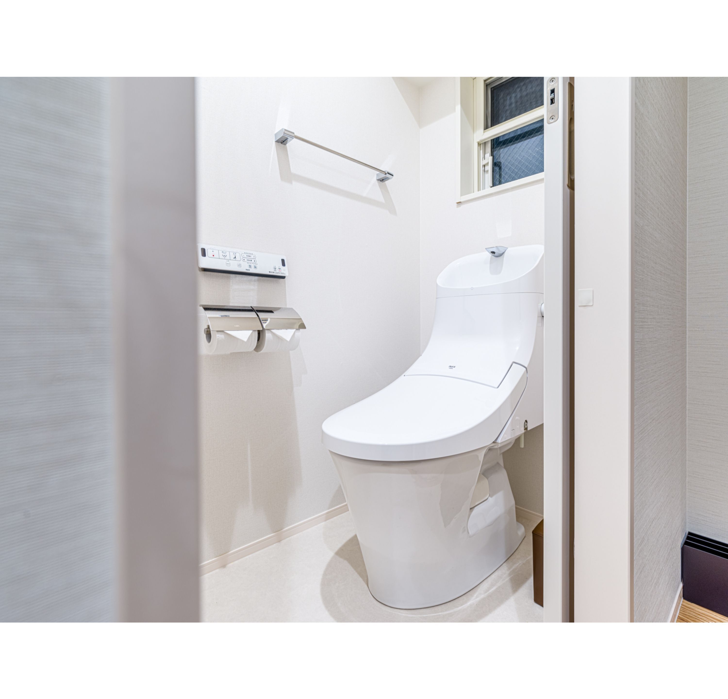 A modern bathroom with a white toilet, a toilet paper holder, and a window above the sink.