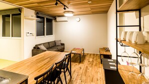 A compact kitchen with wooden flooring, a central dining table with chairs, a built-in shelf with kitchenware, and a window with blinds. - Rakuten STAY HOUSE x WILLSTYLE Haginishitamachi (Hagi)