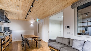 Un intérieur moderne avec un plafond en bois, un coin repas comprenant une table et des chaises, un canapé et un espace cuisine équipé d’appareils électroménagers.