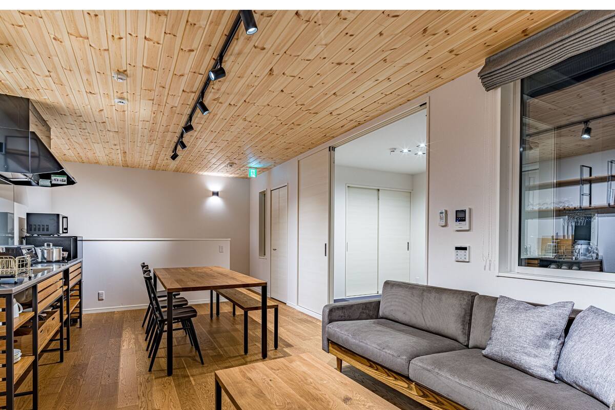 Ein modernes Interieur mit Holzbalkendecke, einem Essbereich mit Tisch und Stühlen, einer Couch und einer Küchenzeile mit Geräten.