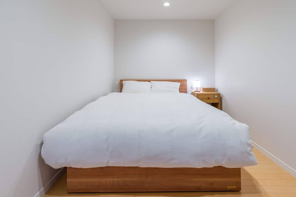 A neatly made bed with white bedding, a wooden headboard, a bedside table with a lamp, and a nightstand.