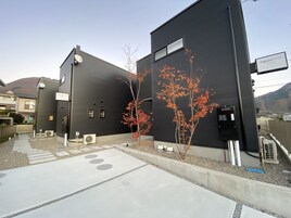 A modern building with a black exterior, a small tree with red leaves, and a clear sky.