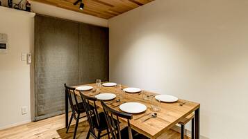 Un espace repas avec une table en bois dressée pour six personnes, des chaises noires et un plafond orné de poutres en bois et doté d’un système d’éclairage sur rails.