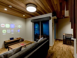 A modern living room with a wooden ceiling, a projection screen displaying icons, a sofa, a table, and a bench.