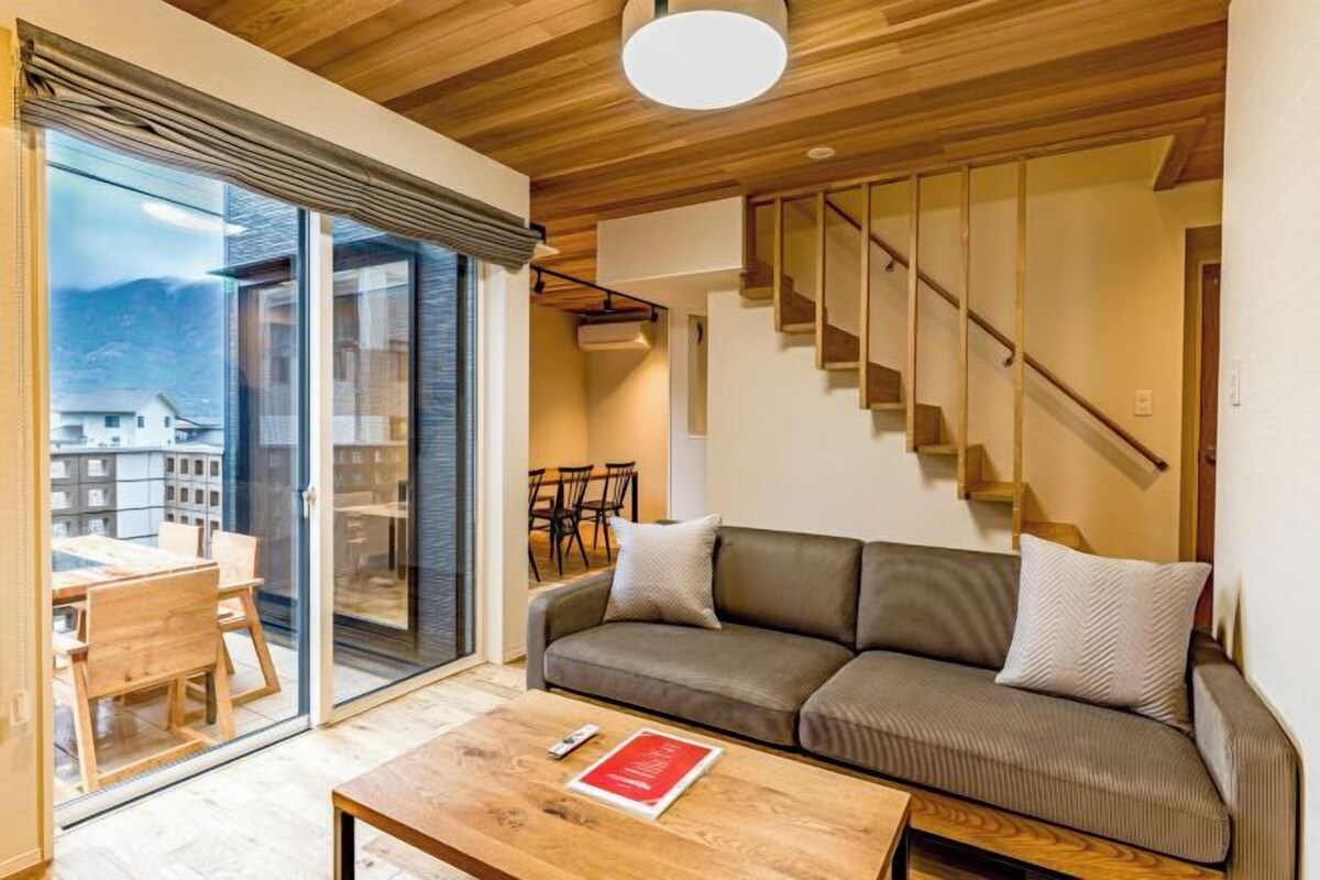A modern living room with a wooden ceiling, a sofa, a coffee table, and a staircase.