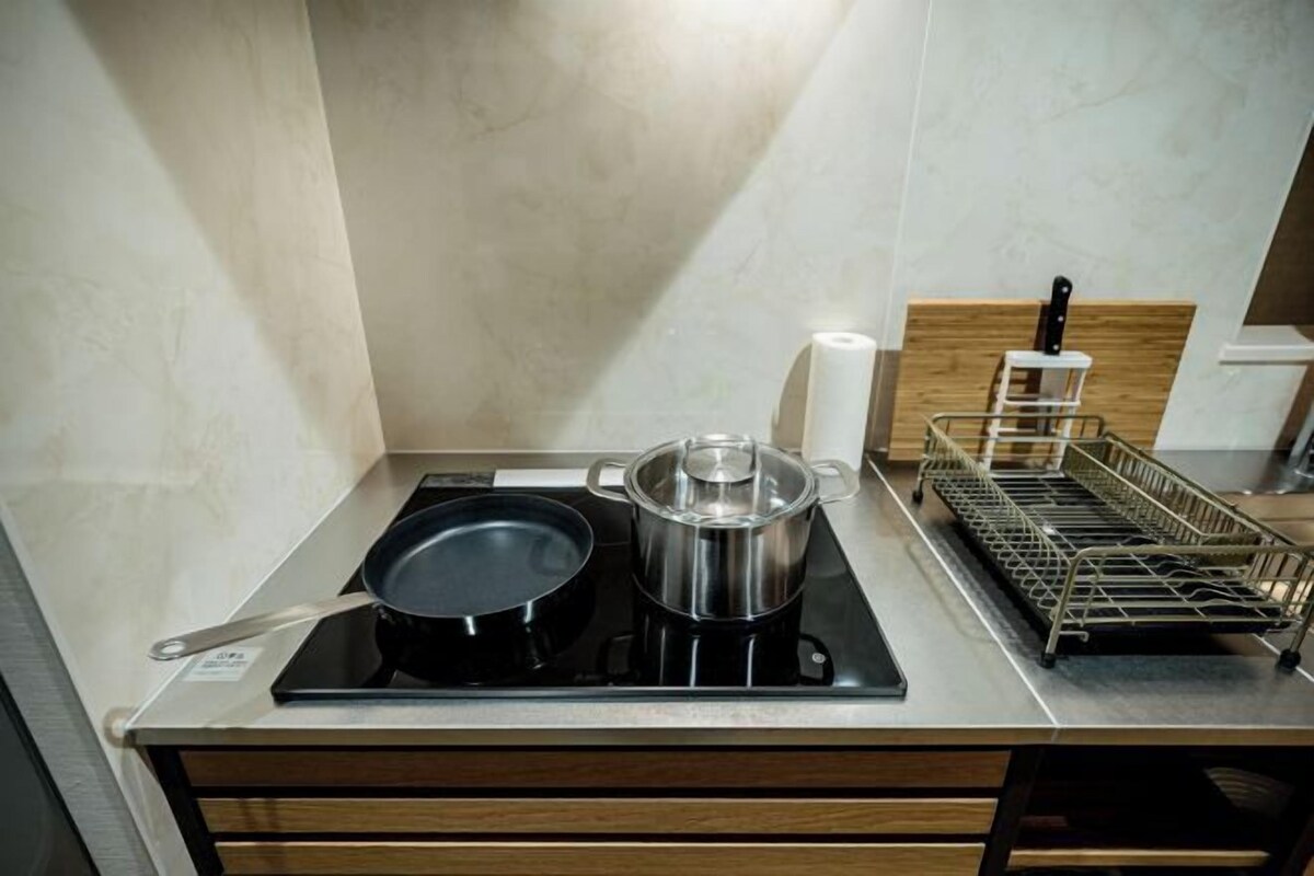 A kitchen with a stove, pots, a dish rack, and a wooden cabinet.