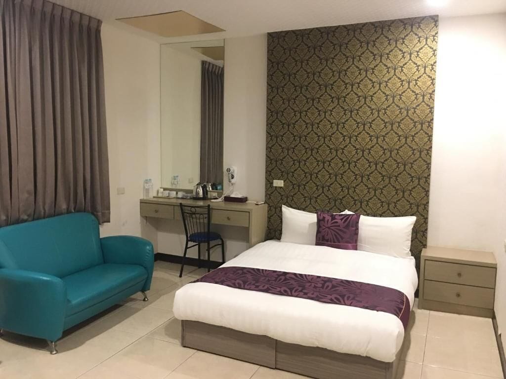 A hotel room with a bed, a desk, a chair, a sofa, and a nightstand.