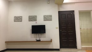 A room with a flat-screen TV mounted on the wall, a bench, and a door leading to a bathroom. - Rural Area Hotel (Zhuqi)