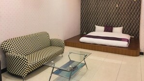 A room with a checkered sofa, a glass coffee table, a bed with a patterned headboard, and an air conditioning unit on the wall. - Rural Area Hotel (Zhuqi)