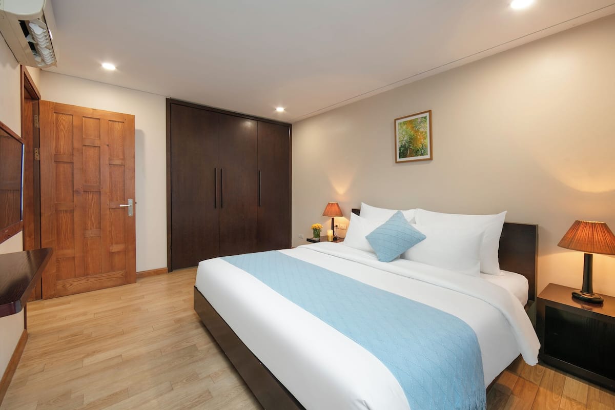 Quarto de hotel com uma cama grande, guarda-roupa de madeira, abajures e um quadro na parede.