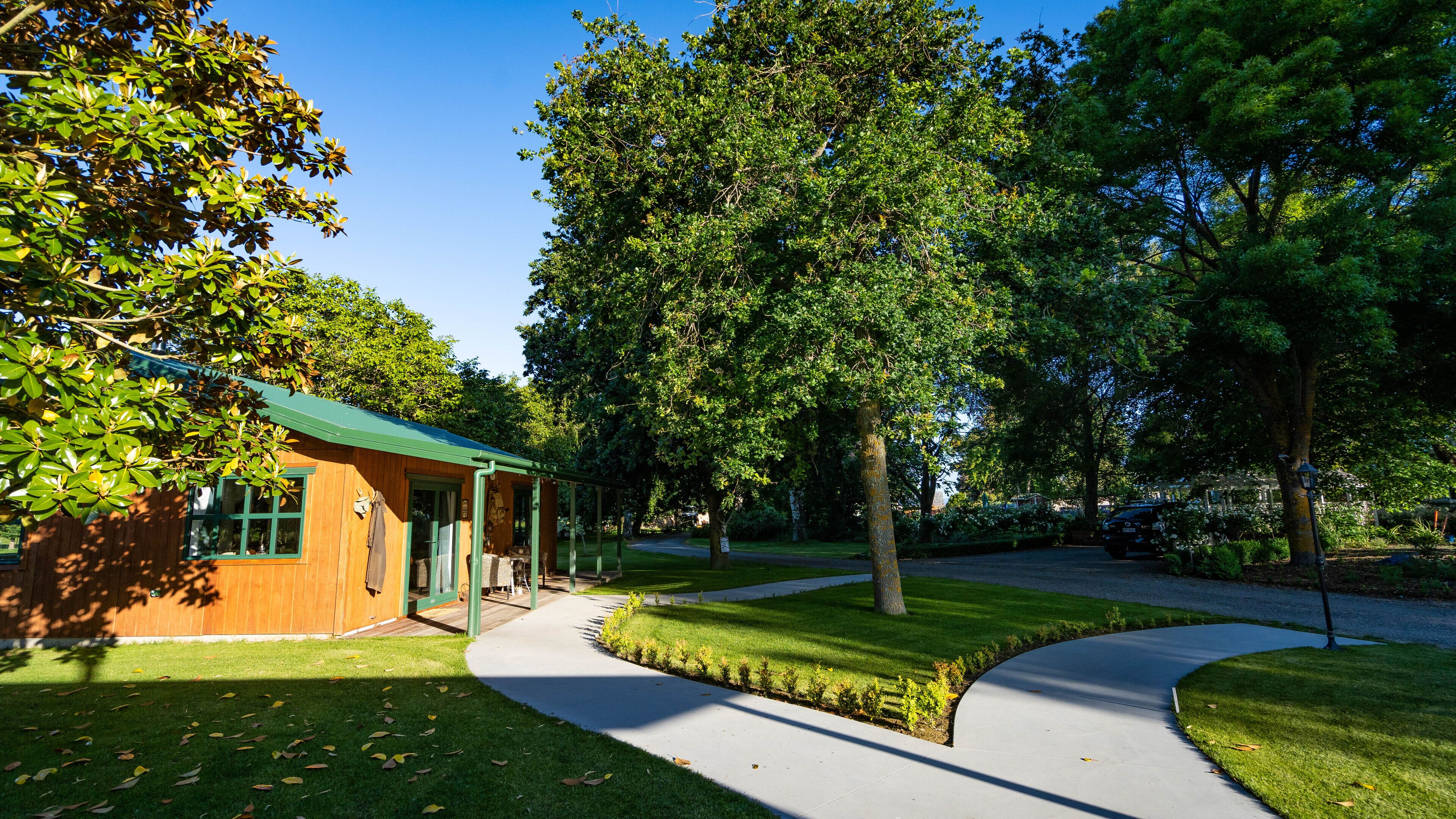 Une cabane en bois avec un toit vert, entourée d’une végétation luxuriante et bordée d’un chemin pavé.