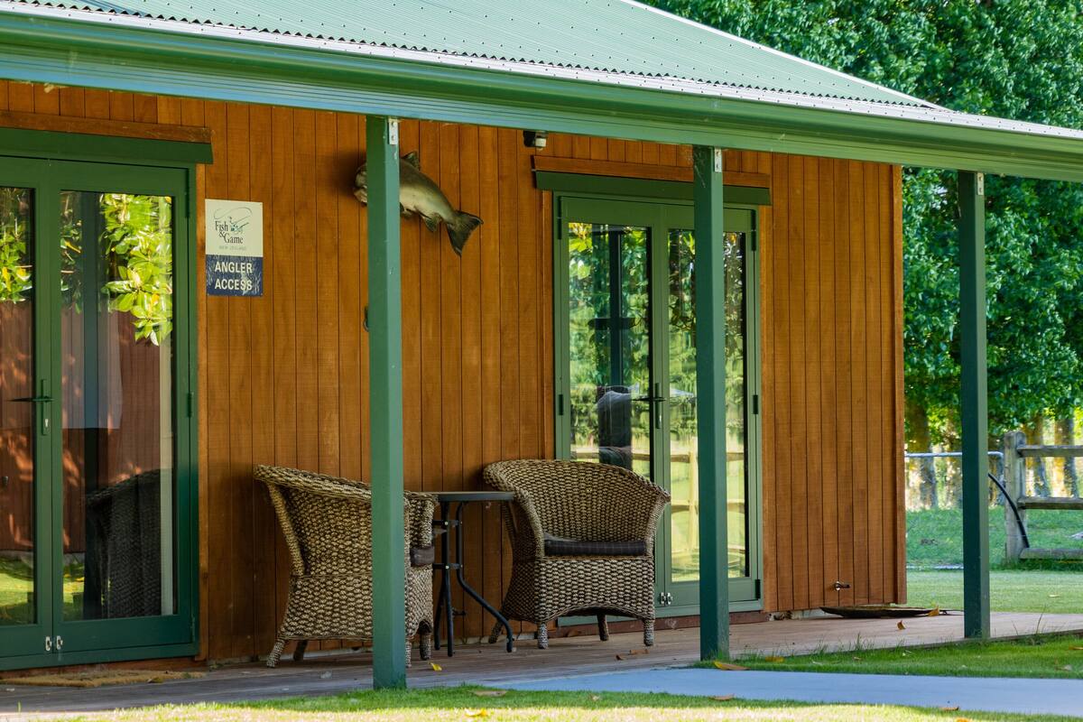 A wooden building with a covered porch, two wicker chairs, and a table.