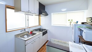 Een kleine keuken met witte kastjes, een roestvrijstalen spoelbak, een fornuis en een magnetron.
