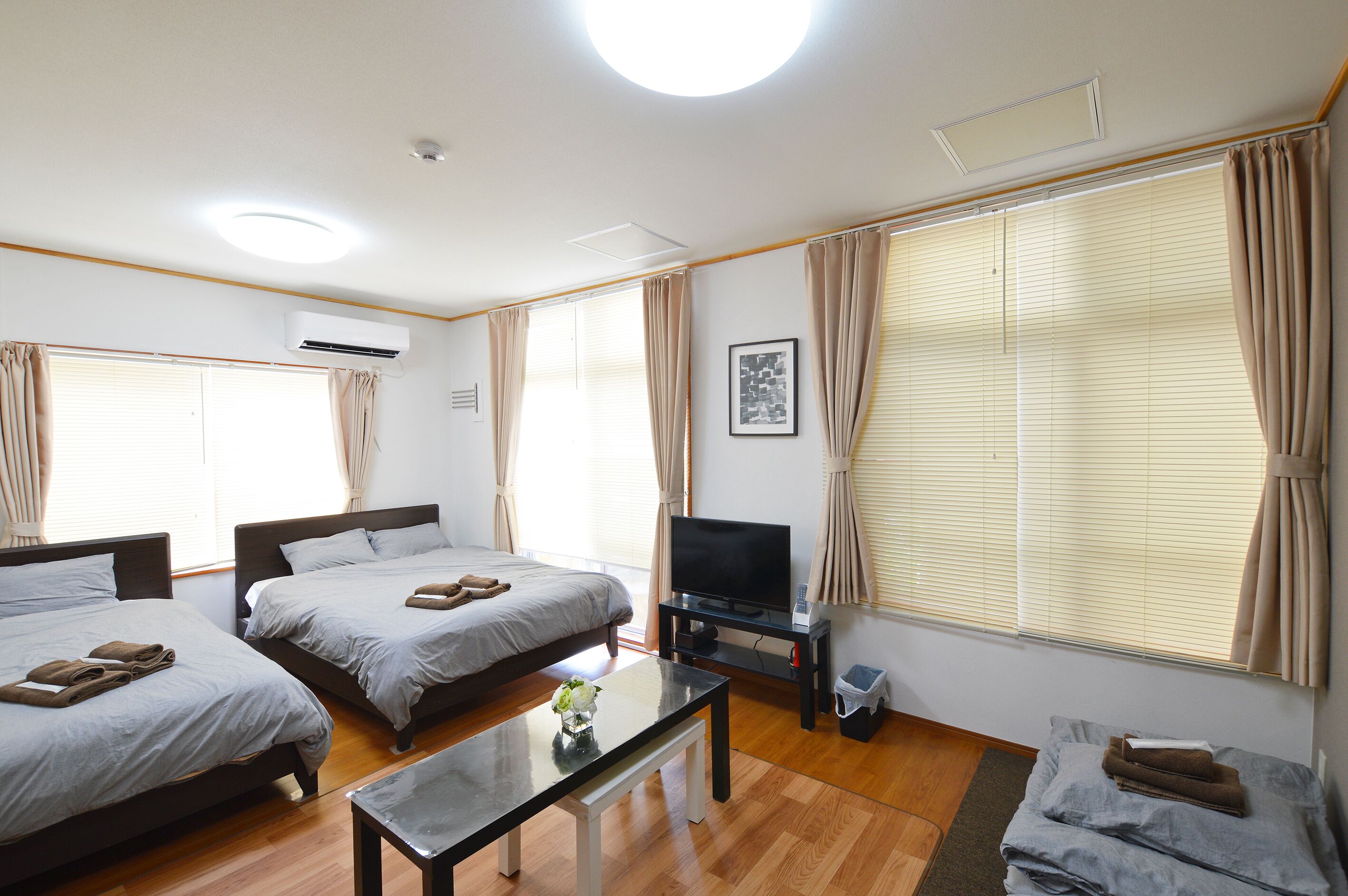 A hotel room with two beds, a flat-screen TV, a small table, and a window with curtains.