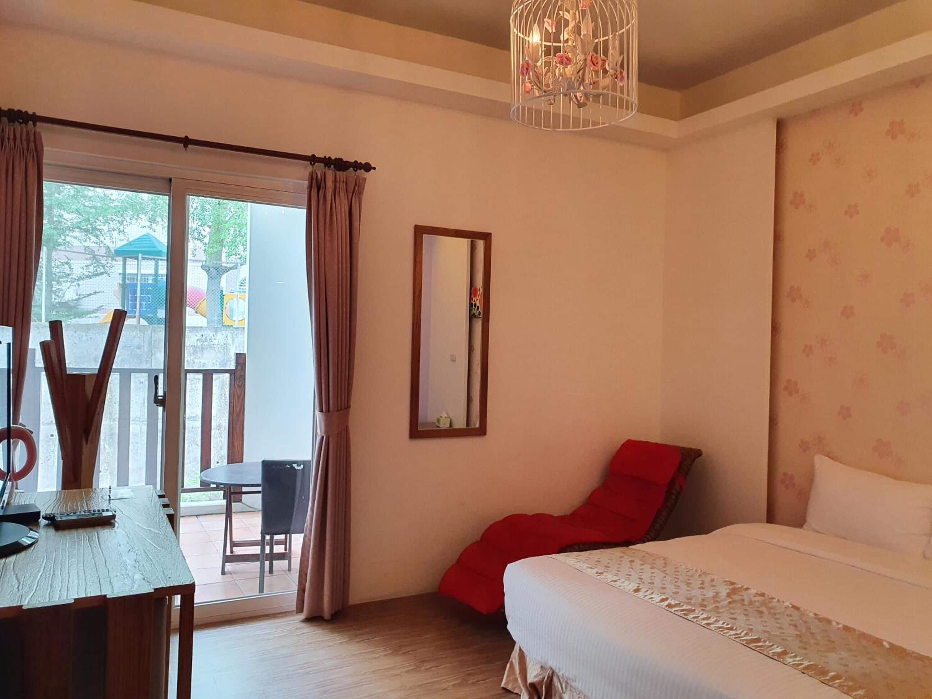 Ein Schlafzimmer mit Bett, Schreibtisch, Stuhl und einem Balkon mit Vorhängen.