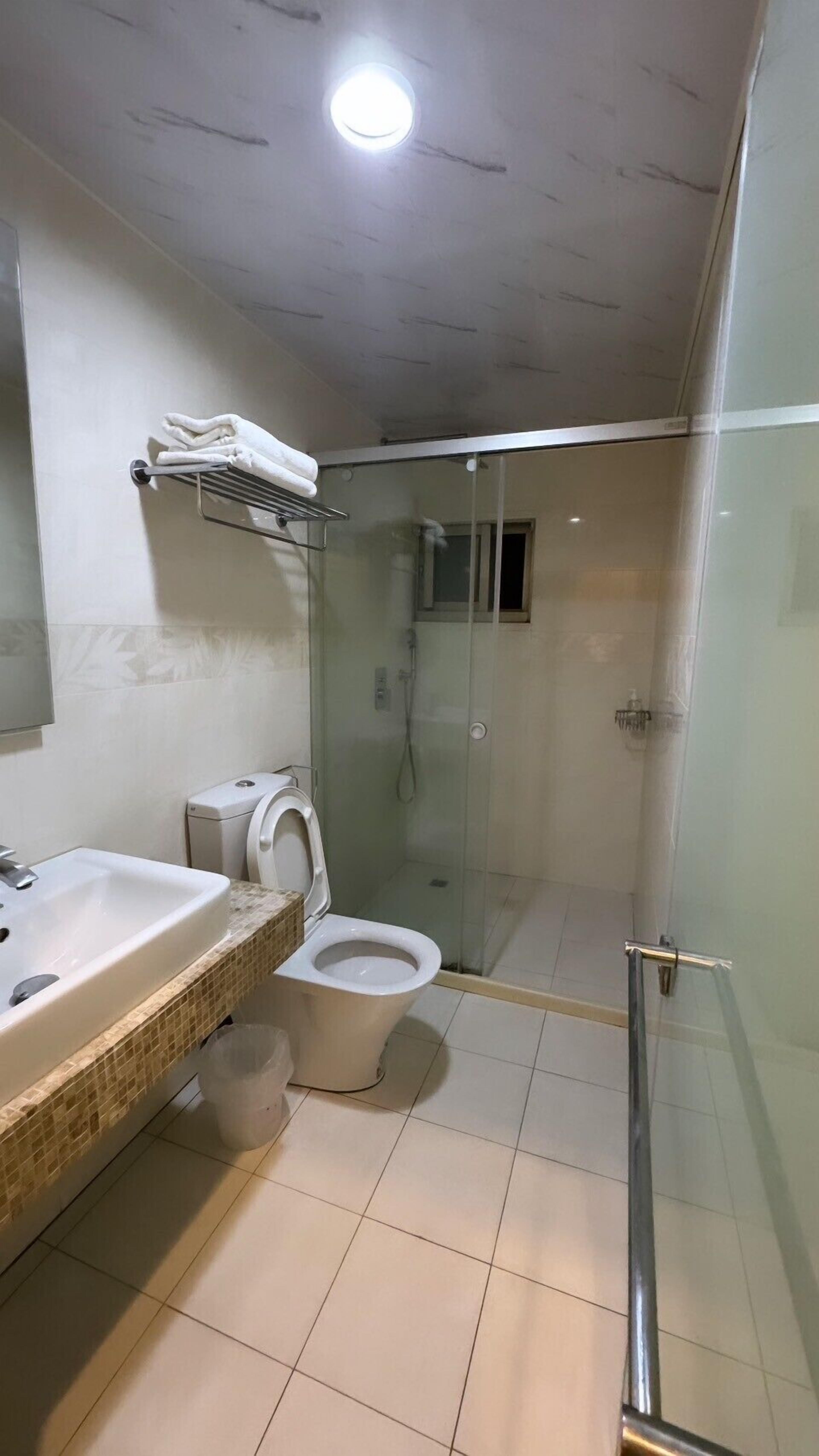 Et moderne badeværelse med et glasbadeværelse, en hvid vask og et toilet.