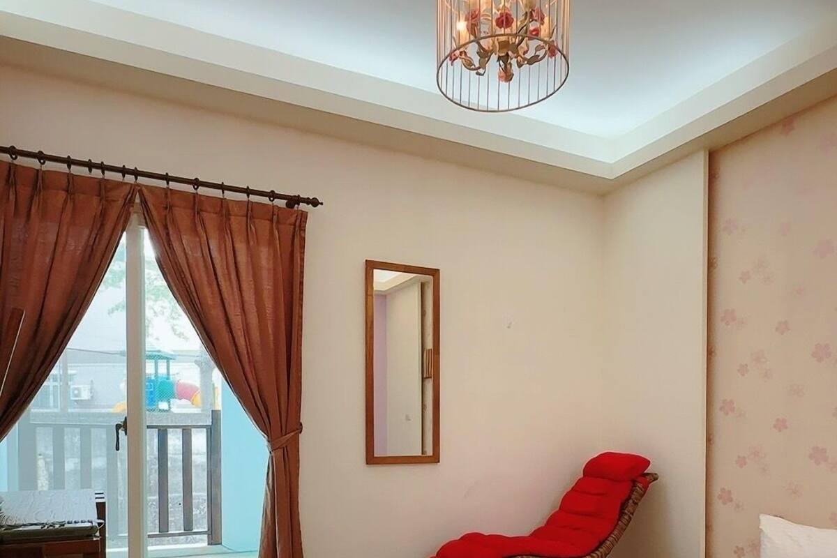 Un dormitorio con cama, una silla roja, un escritorio de madera, un espejo y una araña.