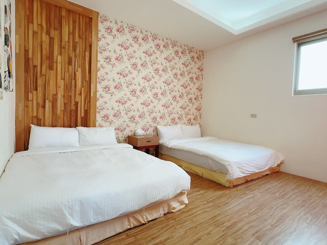 A bedroom with two beds, wooden flooring, a wooden headboard, and a floral wallpaper.