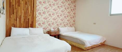 A bedroom with two beds, wooden flooring, a wooden headboard, and a floral wallpaper.