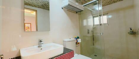 A bathroom with a white sink, a toilet, a glass shower enclosure, and a tiled backsplash.