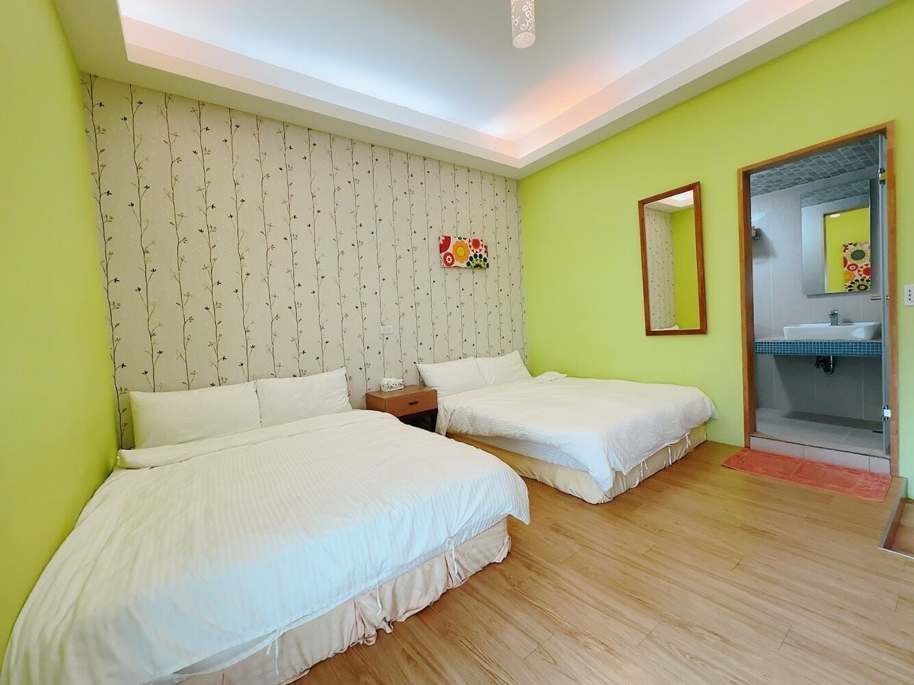 Habitación con dos camas, piso de madera, baño con lavamanos y espejo.