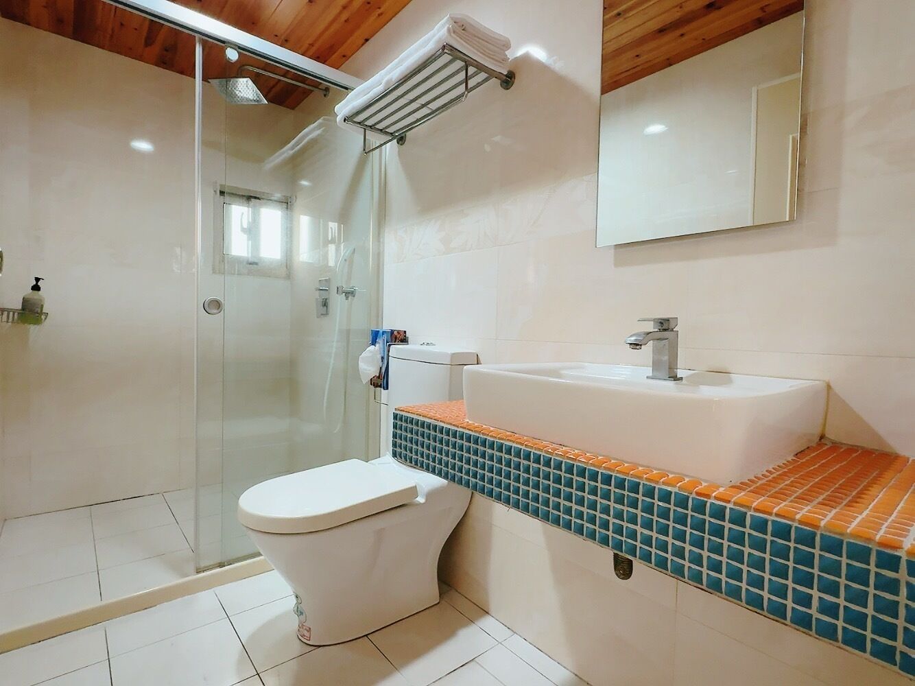 Un baño con cabina de ducha de vidrio, inodoro blanco y lavamanos con encimera de azulejos.