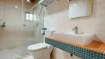 Un baño con cabina de ducha de vidrio, inodoro blanco y lavamanos con encimera de azulejos.