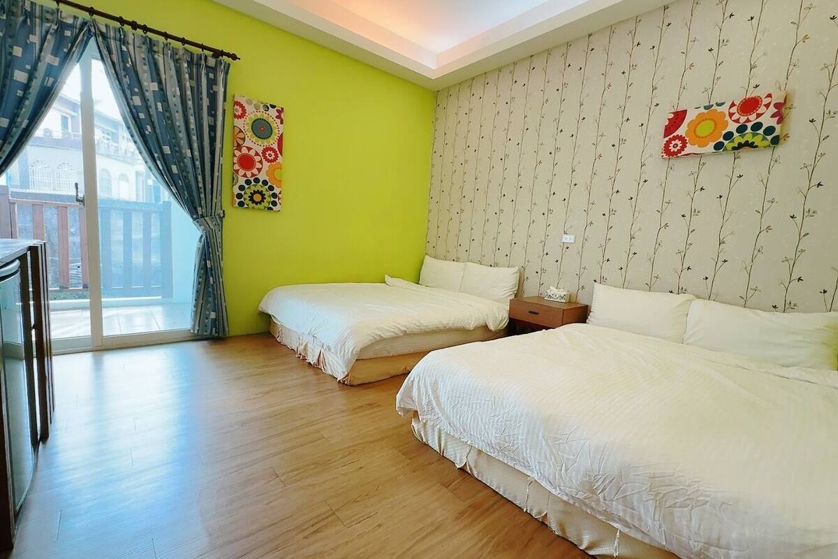 Una habitación con dos camas, piso de madera, puerta corredera de vidrio y pared con estampado floral.