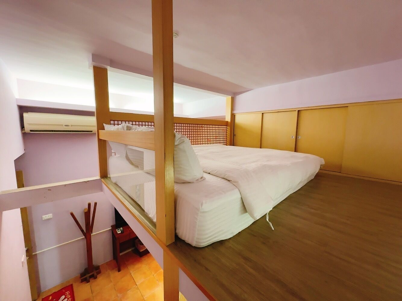 Una habitación pequeña con una cama individual, una mesita y suelo de madera.
