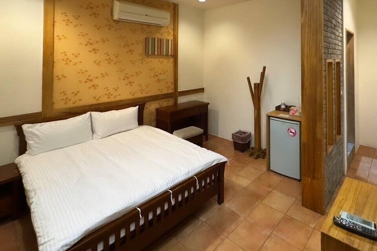 Un dormitorio con una cama grande, un escritorio pequeño, un cubo de basura y un refrigerador pequeño.