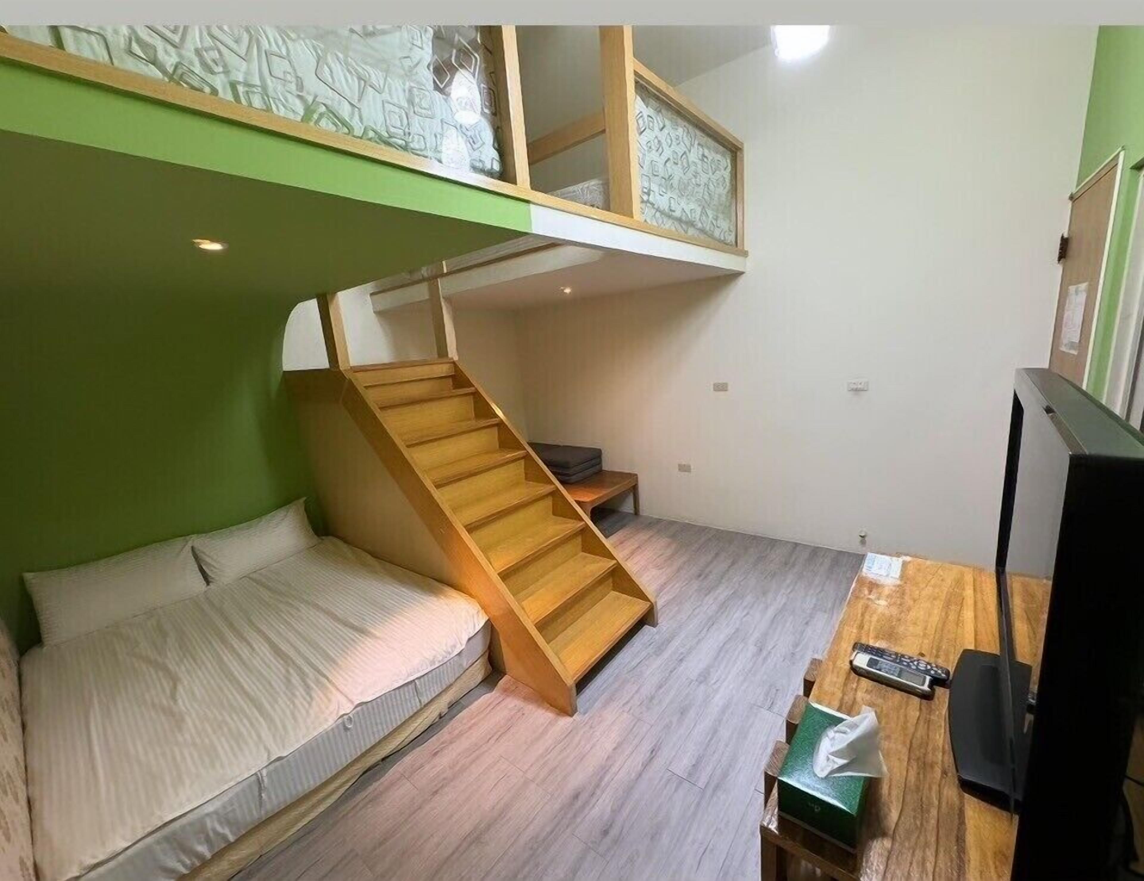 Habitación pequeña con literas, un escritorio, televisión y una escalera que lleva a la litera superior.