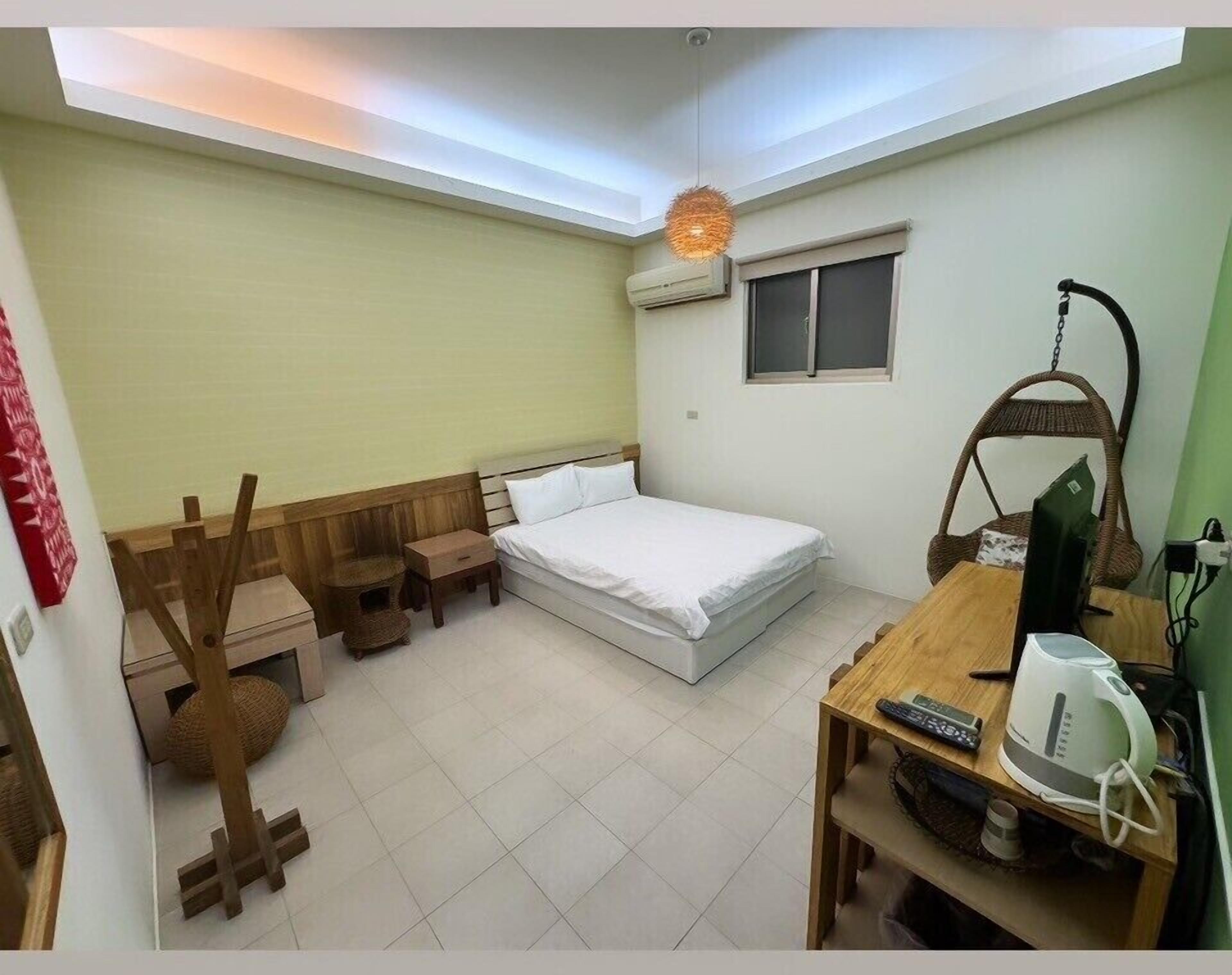 Habitación compacta con una cama individual, una mesita con hervidor, una silla y una lámpara colgante.